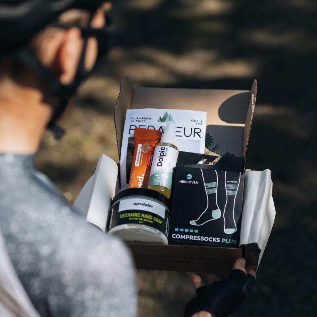 Un cycliste tenant dans les mains la box Pédaleur de septembre 2024 ouverte, permettant de voir son contenu